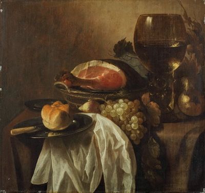 一个带刀和面包卷的锡制拼盘，一个柳条篮子，篮子里有火腿、葡萄和梨，一个半挂着的桌子上有一桶葡萄酒